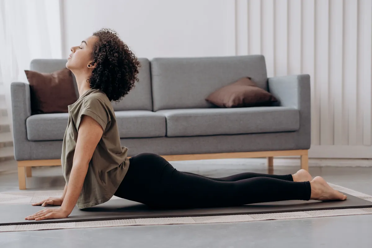 A woman stretches on an exercise mat in a bright living room.