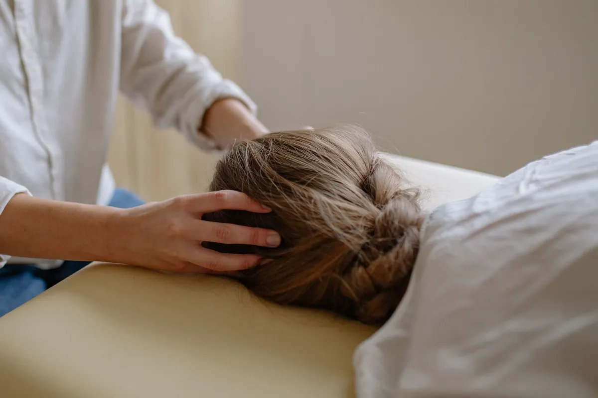 A practitioner's hands gently cradle the head of a person resting on a padded table.
