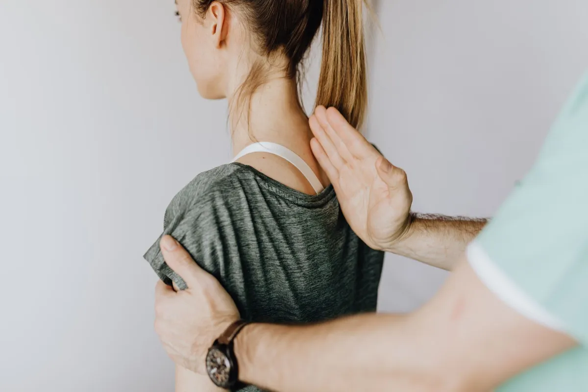A chiropractor's hands gently assess a patient's upper spine and shoulder.