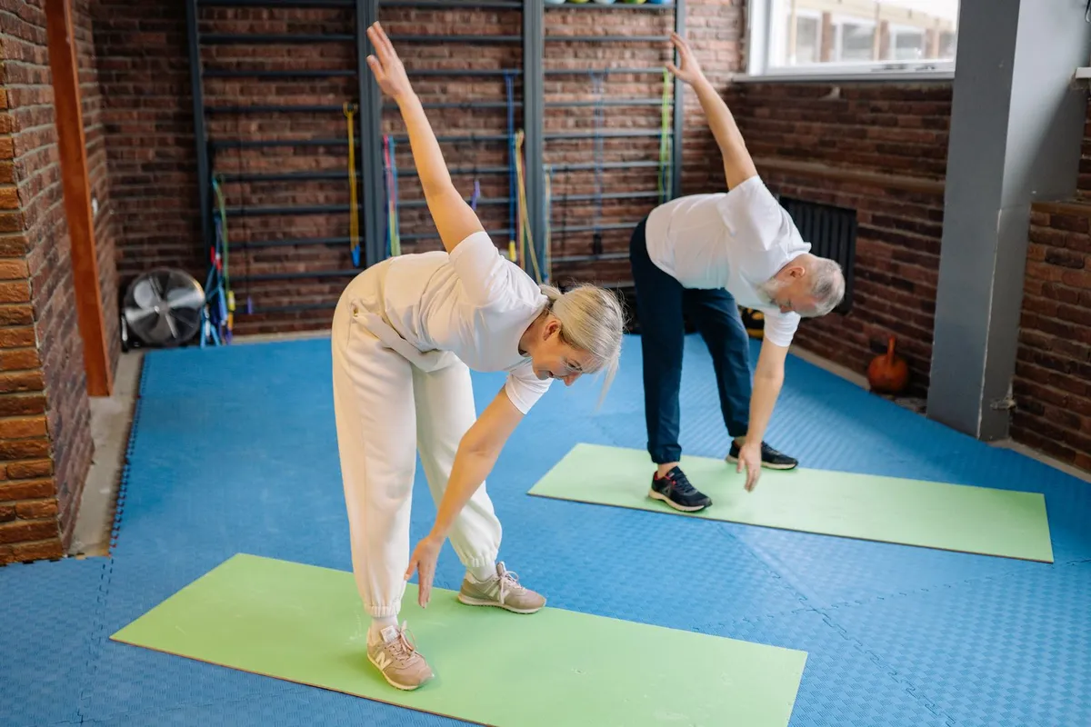 Two older adults do gentle standing stretches during a wellness exercise session.